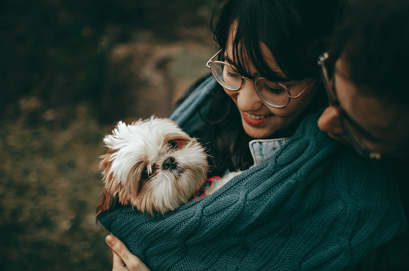 A couple carrying their dog and hugging it
